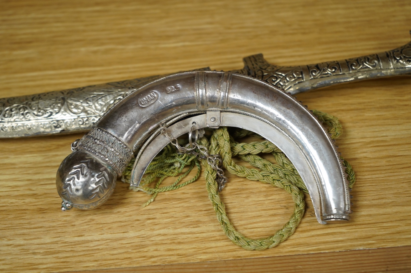 An Omani silver spice box in the form of a curved powder flask, together with a Moroccan dagger Jambiya with nickel hilt and sheath, both 20th century. Condition - fair.
